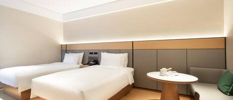 A modern hotel room with two beds, a round wooden table, and a sofa.