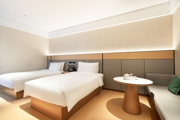 A modern hotel room with two beds, a round wooden table, and a sofa.