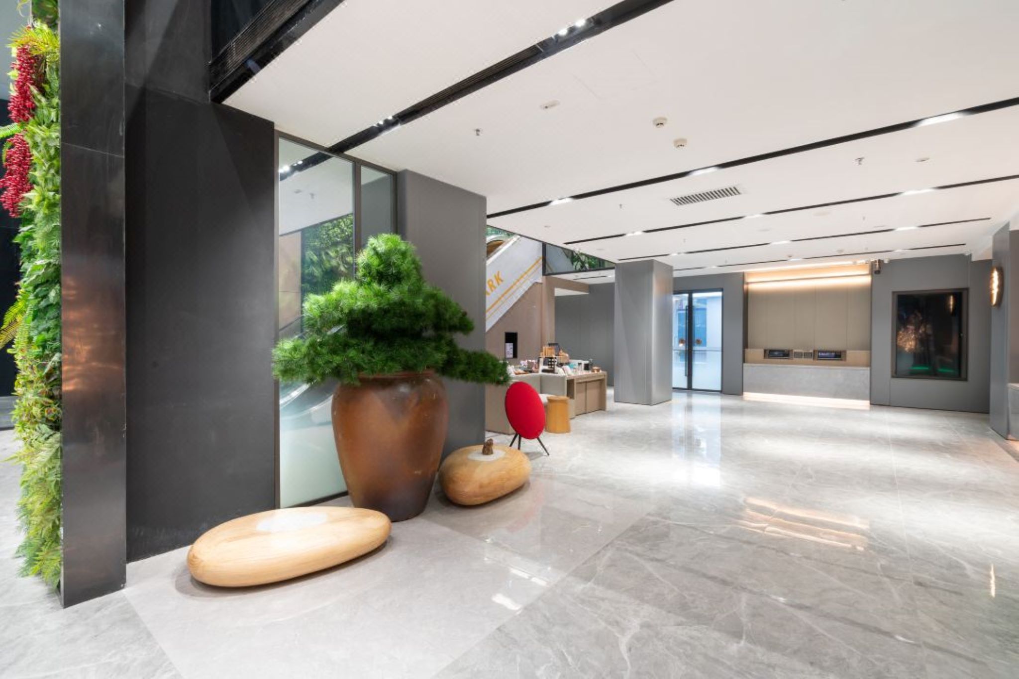 A modern lobby with a large potted plant, a reception desk, and a staircase.