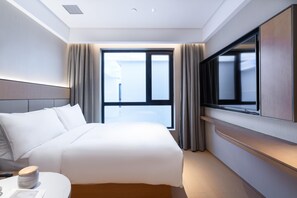 A hotel room with a bed, a TV, a window with curtains, and a view of the outside.