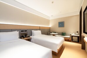 A hotel room with two beds, a small table, a sofa, a TV, and a minibar.