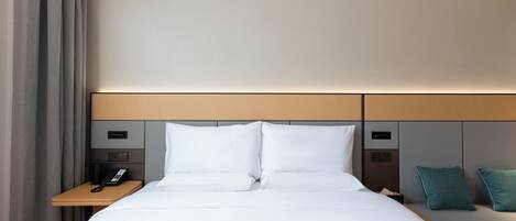 A hotel room with a large bed, a bedside table with a phone, and a nightstand with a lamp.