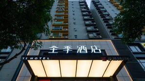 Ein Hotel Eingang mit einem Schild in Englisch und Chinesisch, ein großes, beleuchtetes Schild mit 'HAPPY NEW YEAR' und eine moderne Gebäudefassade mit mehreren Balkonen.