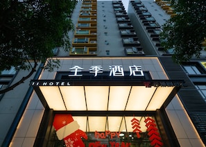 A hotel entrance with a sign in both English and Chinese, a large illuminated sign with 'HAPPY NEW YEAR,' and a modern building facade with multiple balconies.
