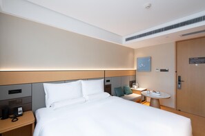A hotel room with a large bed, bedside table, a small round table, a wall-mounted TV, and a door with a lock.
