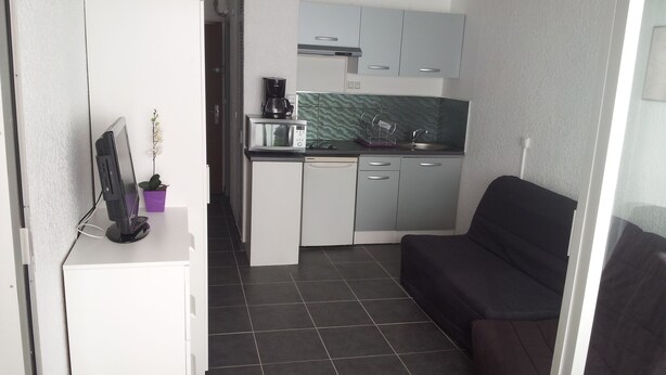 A compact kitchenette with a microwave, coffee maker, and sink. A small desk with a computer monitor and a potted plant is visible. - WATERFRONT STUDIO APARTMENTS CARNON PLAGE NEAR LA GRANDE MOTTE (CARNON PLAGE)