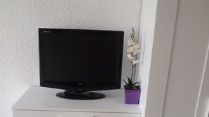 A white cabinet with a flat-screen TV on top, a small purple plant, and a drawer with a glass window. - WATERFRONT STUDIO APARTMENTS CARNON PLAGE NEAR LA GRANDE MOTTE (CARNON PLAGE)