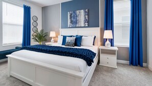 A bedroom with a large bed, two bedside tables, a nightstand, a wall-mounted artwork, and a potted plant. - New Storey Lake 6BR/5BA-Pool/ Spa/ Game Room (Kissimmee)