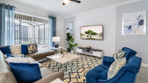 A modern living room with a sofa, armchair, coffee table, and a TV on the wall. - New Storey Lake 6BR/5BA-Pool/ Spa/ Game Room (Kissimmee)