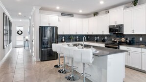 A modern kitchen with white cabinets, stainless steel appliances, and a central island with bar stools. - New Storey Lake 6BR/5BA-Pool/ Spa/ Game Room (Kissimmee)