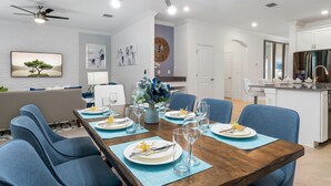 A dining area with a wooden table set for six, blue chairs, and a modern ceiling fan. - New Storey Lake 6BR/5BA-Pool/ Spa/ Game Room (Kissimmee)