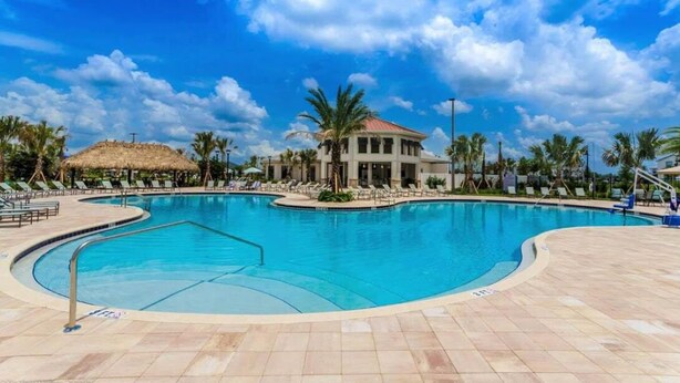 A swimming pool with lounge chairs and a building with a red roof. - New Storey Lake 6BR/5BA-Pool/ Spa/ Game Room (Kissimmee)