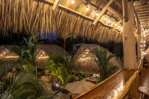 A thatched-roof structure with seating and umbrellas, surrounded by palm trees.