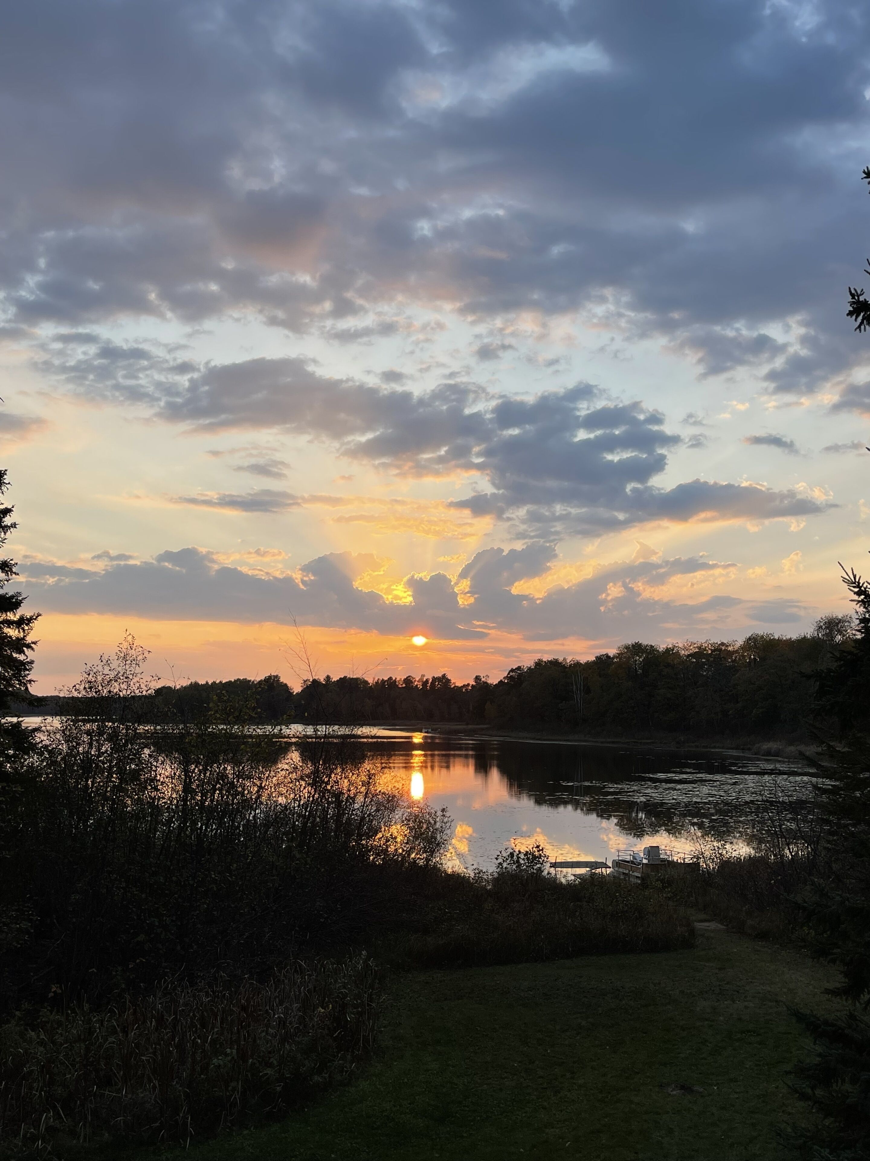 Un coucher de soleil sur un lac paisible, bordé d’arbres et doté d’un quai.