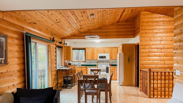 L’intérieur d’une cabane en rondins comprend un coin repas, une cuisine et un salon avec un canapé et des fauteuils.