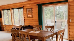 Une salle à manger en bois, avec une table et des chaises, de grandes fenêtres et une vue sur l’extérieur.
