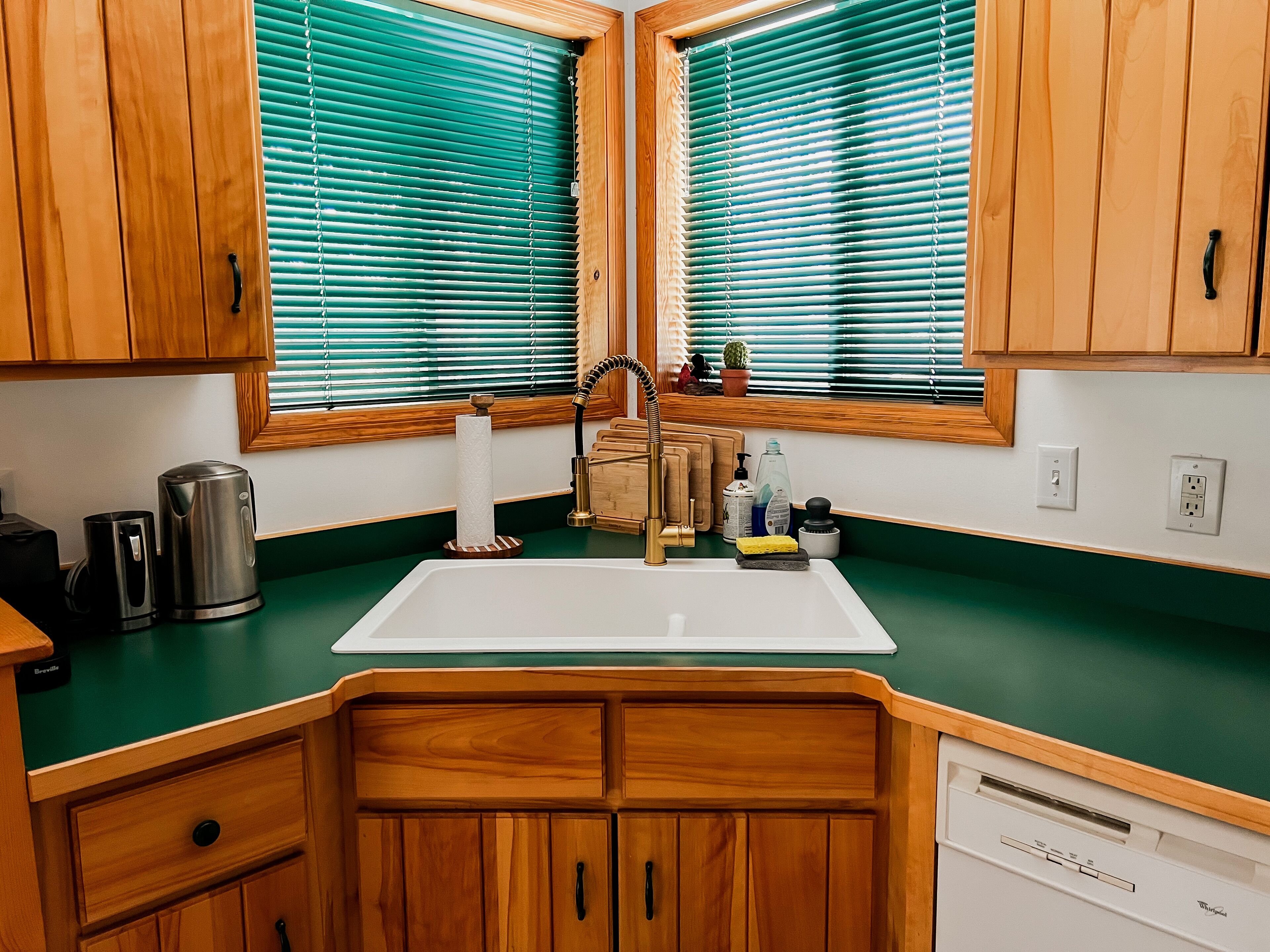 A kitchen with wooden cabinets, a stainless steel kettle, a sink, and a window with blinds.