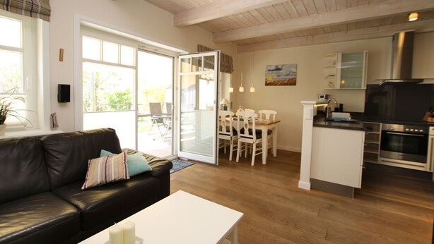 A modern living room with a black leather sofa, a white coffee table, and a dining area with white chairs. - Comfortable 5-star vacation home with approx. 55 sqm living space on the first floor (Wyk auf Foehr)