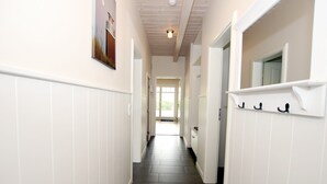 A narrow hallway with white wainscoting, a dark wooden floor, and a door at the end leading to a bright room. - Comfortable 5-star vacation home with approx. 55 sqm living space on the first floor (Wyk auf Foehr)