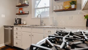 A kitchen with white cabinets, a stainless steel dishwasher, a granite countertop, and a window above the sink.