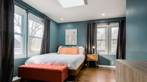 A bedroom with a bed, a nightstand, a bench, and a window with curtains.