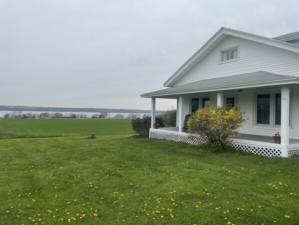 A white house with a porch and a lawn with yellow flowers. - Newly Renovated Farmhouse Finger Lakes (Romulus)