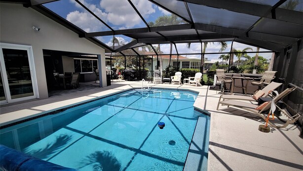 A swimming pool with a glass ceiling, surrounded by lounge chairs and a patio area.