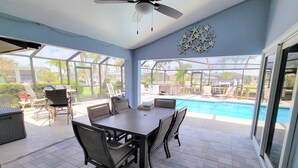 A covered patio area with a pool, outdoor furniture, and a ceiling fan.