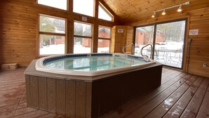 A wooden cabin with a hot tub, large windows, and a sliding glass door.