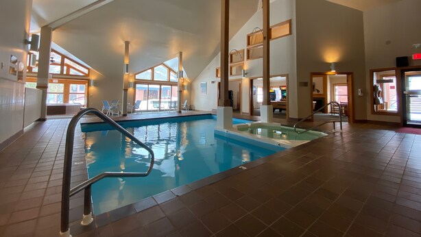 An indoor swimming pool with a clear view of the pool area, a pool ladder, and a seating area with chairs.