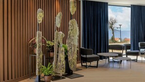 A modern lobby with wooden paneling, a large window with a view, and a seating area with tables and chairs. - AC Hotel Saint-Julien-en-Genevois (Saint-Julien-en-Genevois)