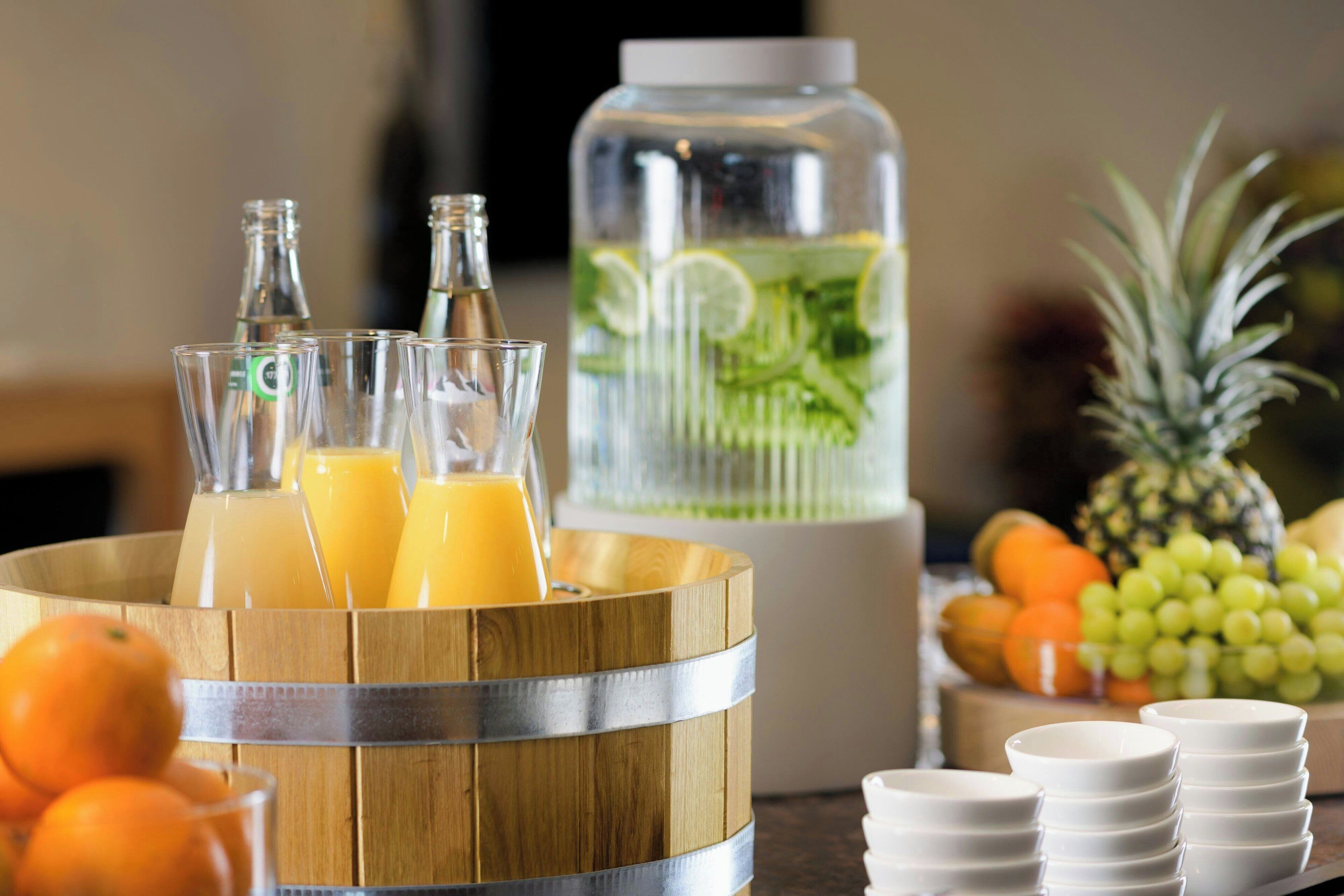 Desayuno con botellas de jugo, un dispensador grande de agua y frutas frescas.
