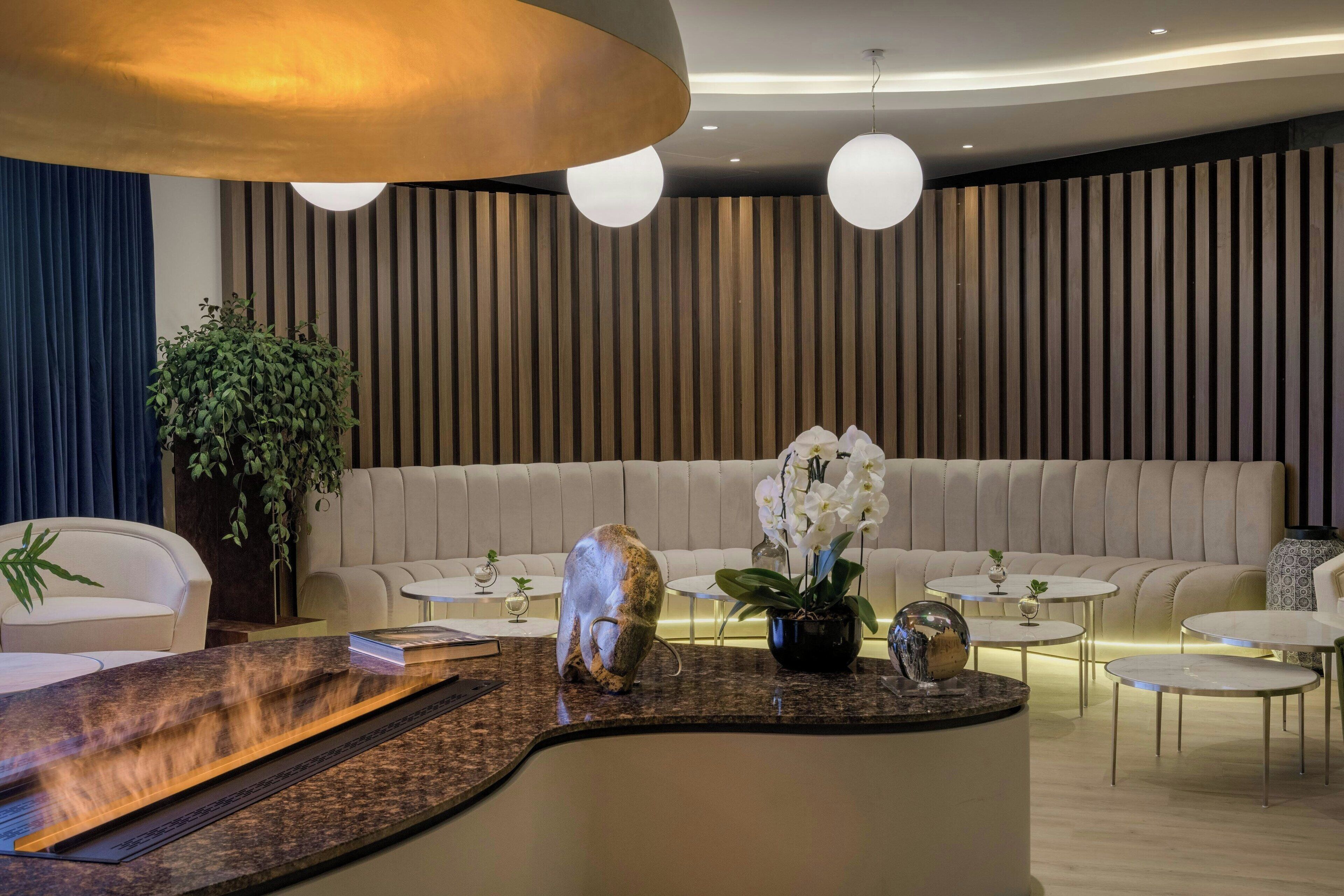 A modern reception area with a curved counter, a large potted plant, and a seating area with a sofa and armchairs.
