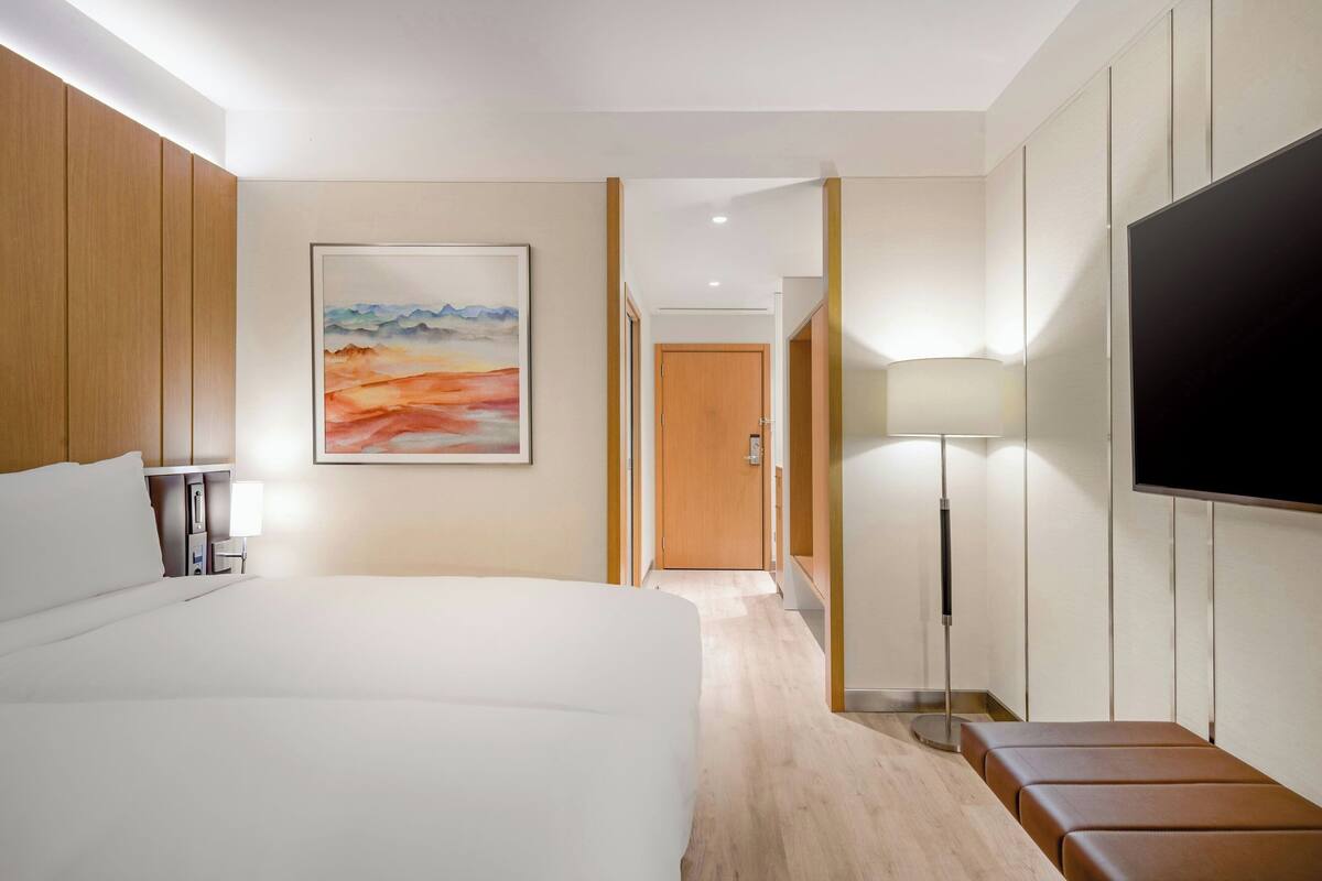 Habitación de hotel con una cama grande, televisión de pantalla plana, mesita de noche, lámpara y un cuadro en la pared.