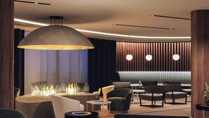 A modern lounge area with a central fire feature, comfortable seating, and ambient lighting. - AC Hotel Saint-Julien-en-Genevois (Saint-Julien-en-Genevois)