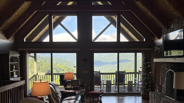 Ein geräumiges Wohnzimmer mit hoher Decke, großen Fenstern mit Blick auf die Berge, einem Kamin und einer gemütlichen Sitzecke.
