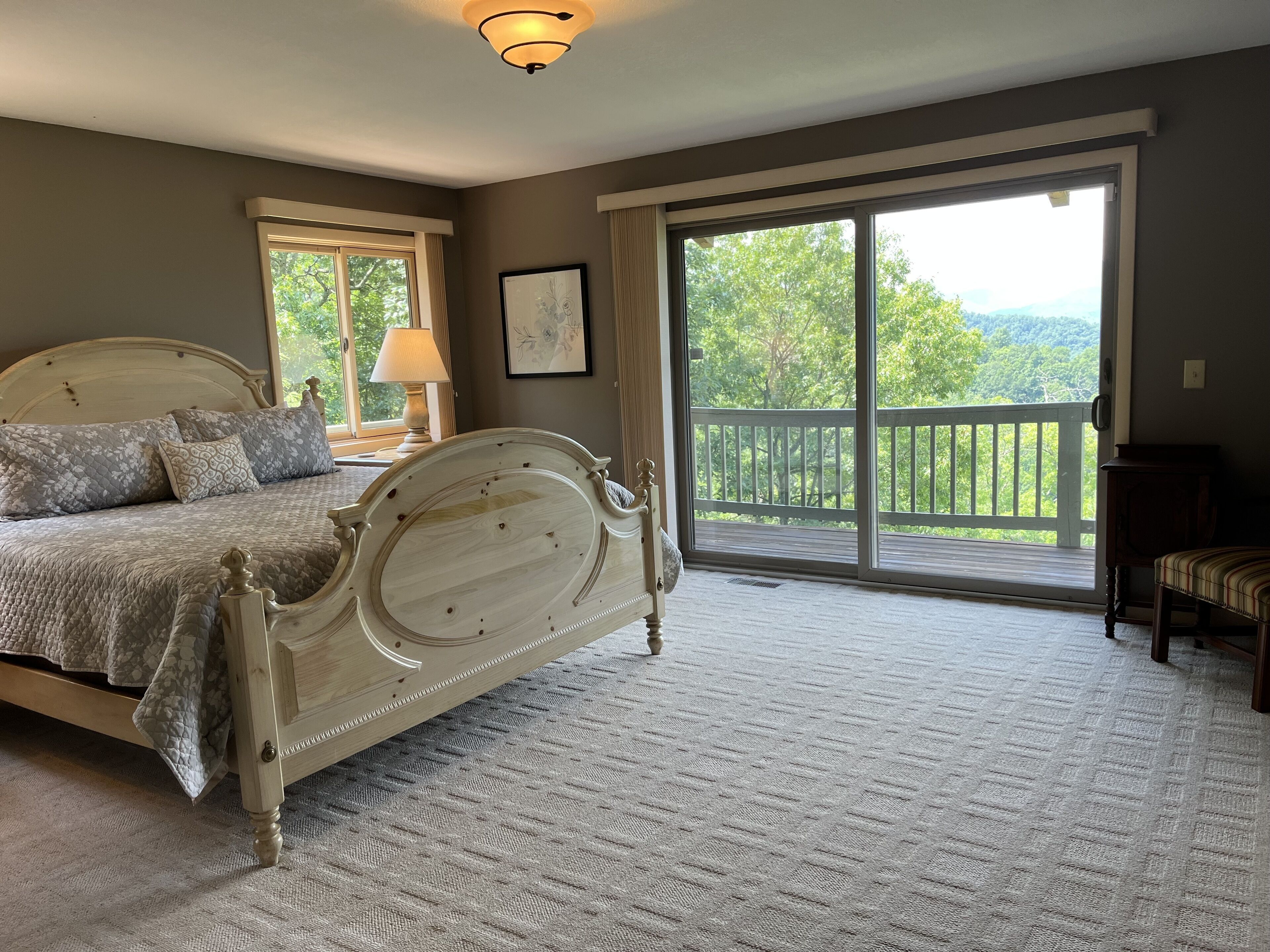 A bedroom with a large bed, a nightstand, a lamp, a framed picture, and a view of a balcony with a railing.