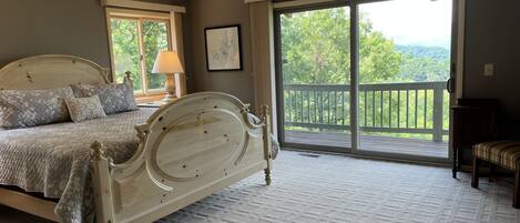 A bedroom with a large bed, a nightstand, a lamp, a framed picture, and a view of a balcony with a railing.