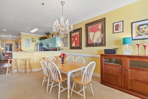 Un coin repas avec une table en bois et des chaises blanches, un lustre et des œuvres d’art accrochées aux murs.