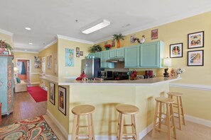 Une cuisine avec des meubles de couleur turquoise, un îlot central doté de tabourets et divers appareils de cuisine.