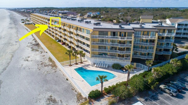 A multi-story hotel with a pool, located near a beach.