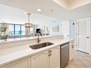 A modern kitchen with a large island, a built-in dishwasher, and a view to the living area.
