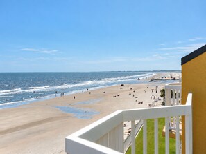A beach view from a balcony with a railing, a sandy beach, and the ocean.