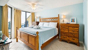 A hotel room with a wooden bed, a dresser, a ceiling fan, and a view of the outside.