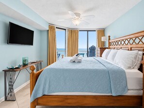 A hotel room with a bed, a flat-screen TV, a desk with a lamp, and a view of the ocean.