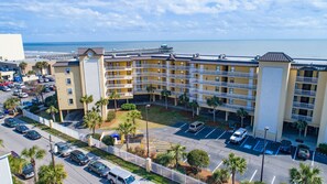 A multi-story hotel with a parking lot and a view of the beach.