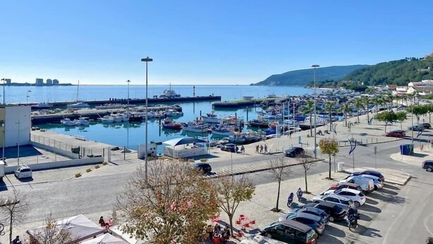 Ein Yachthafen mit vertäuten Booten, einem Parkplatz und freiem Blick auf das Meer.