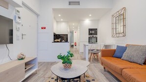 Ein modernes Wohnzimmer mit einer Couch, einem Couchtisch mit Pflanze und einem Fernseher auf einem Holzregal.
