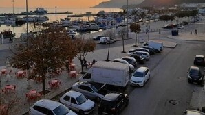 Ein Hafen mit vertäuten Booten, ein Parkplatz mit Autos und ein Sonnenuntergang im Hintergrund.