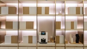 Ett modernt hotellrum med en centralt placerad kaffemaskin, snyggt ordnade förvaringslådor och en dekorativ ängelsfigur på väggen.